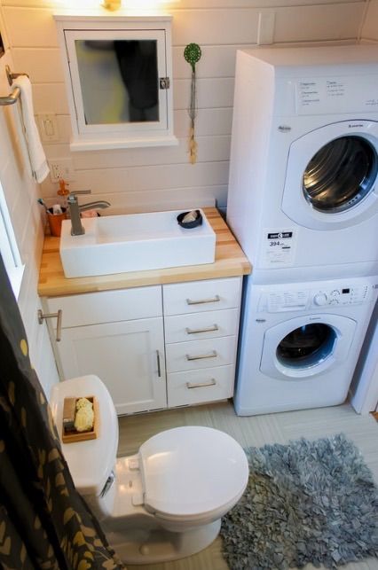 a tiny bathroom with a washing machine and a dryer, a small white vanity, a sink, a toilet plus beadboard on the walls is cool