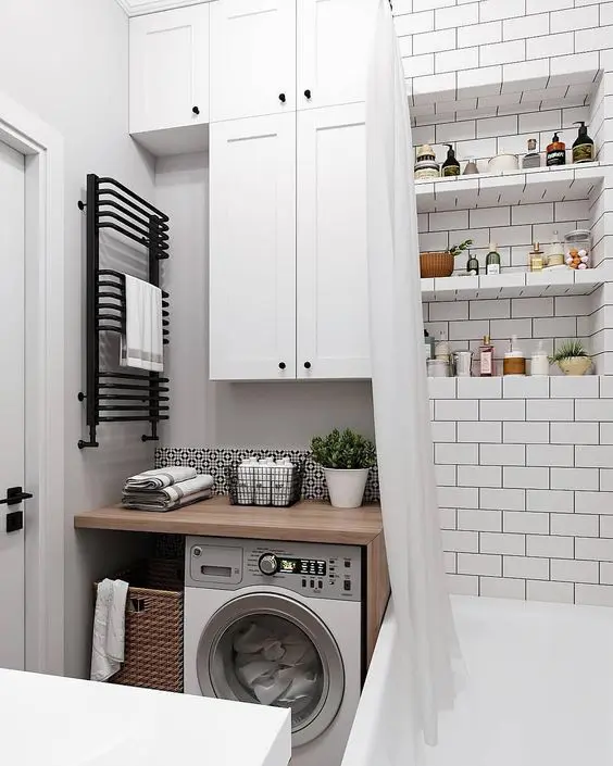a tiny neutral bathroom clad with subway tiles, with a tub, a built in washing machine, some storage cabinets and a sink shows how to effectively use the space