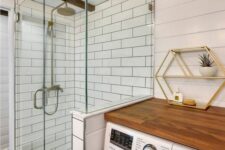 43 a white farmhouse bathroom clad with beadboard and white subway tiles, a washing machine with a butcherblock countertop, a shower space and wooden beams