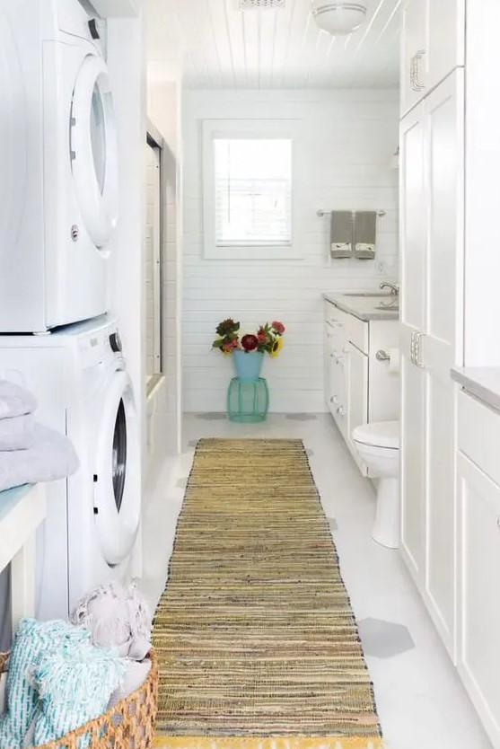 a white farmhouse bathroom clad with beadboard, with a large vanity, a bathtub and a stacked washing machine and a dryer