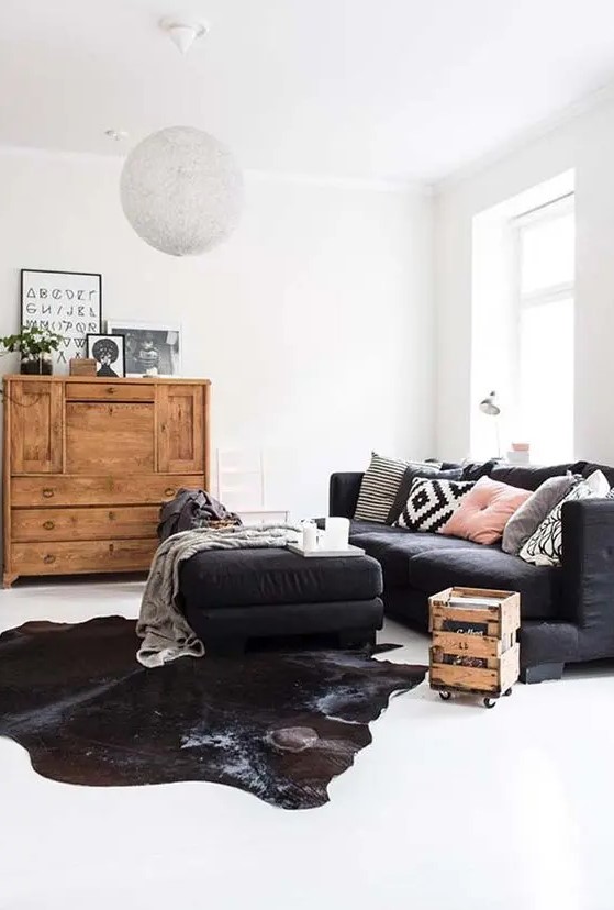 a Nordic living room with a black sofa and a large ottoman, a stained bureau, a crate on casters and potted plants