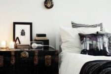 a Scandinavian bedroom with a bed, monochromatic bedding, a black vintage chest, candles, some decor and magazines