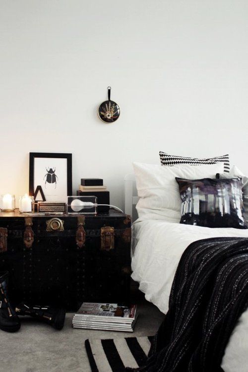 a Scandinavian bedroom with a bed, monochromatic bedding, a black vintage chest, candles, some decor and magazines