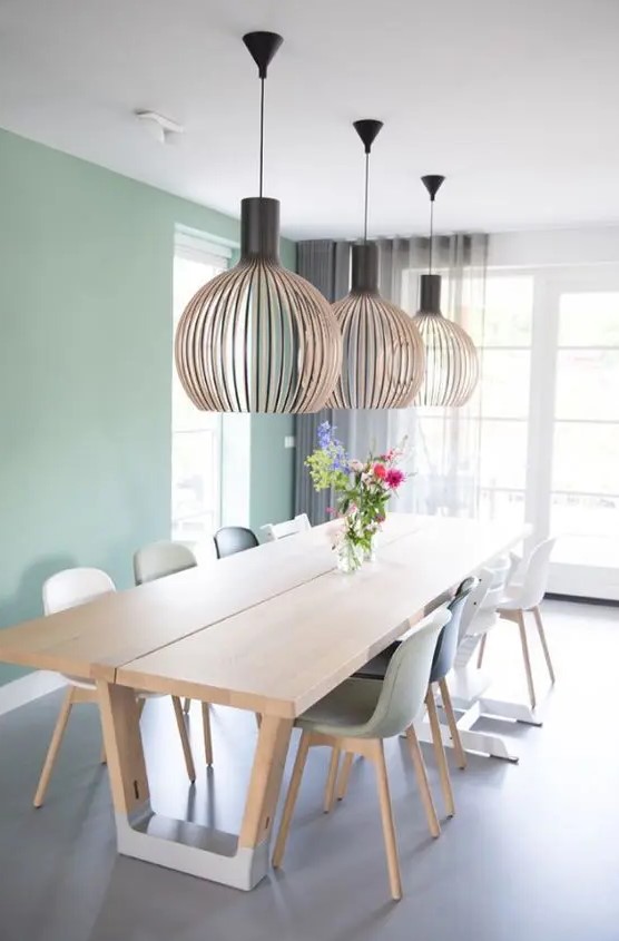 a Scandinavian dining room with a mint green accent wall, a stained table and mismatching chairs plus oversized lamps