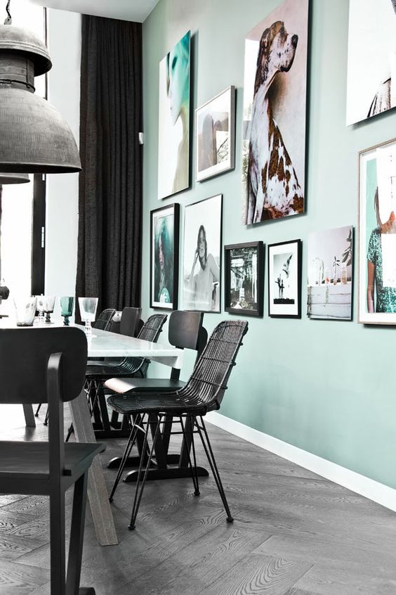 a Scandinavian dining space with a mint green accent wall with a gallery wall, a dining table and mismatching chairs