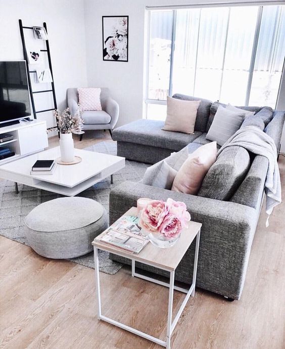 a Scandinavian living room with a grey sectional, a TV and a TV unit, a tiered coffee table, pink pillows and blooms