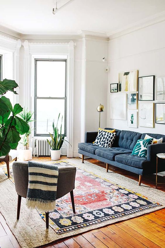 a Scandinavian living room with a navy sofa, a gallery wall, layered rugs, a grey chair, potted plants is a cozy space