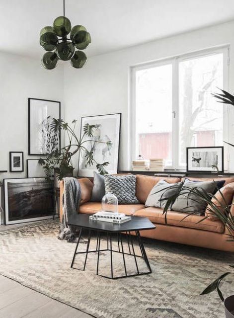 a Scandinavian living room with a tan leather couch, printed pillows, black and white artwork, a black coffee table and a green chandelier