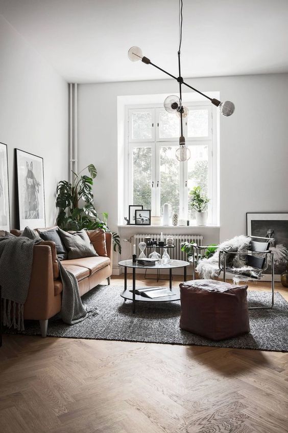 a Scandinavian living room with a tan leather sofa and pouf, a chair with faux fur, a coffee table, a chandelier and black and white artwork