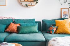 a Scandinavian living room with a turquoise sofa, a wicker coffee table, bold pillows and a round mirror is cool