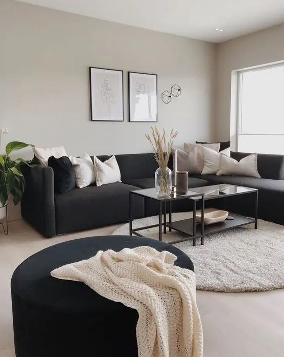 a Scandinavian living room with grey walls, a black sectional, a tiered coffee table, a black pouf and a potted plant
