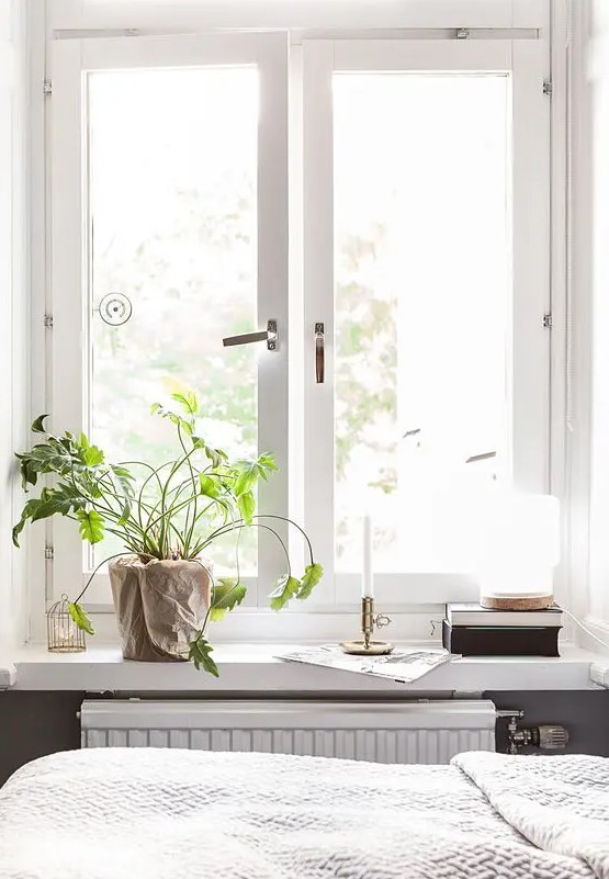 a Scandinavian space with a casement window, a windowsill styled with potted greenery, candles, books and a lantern