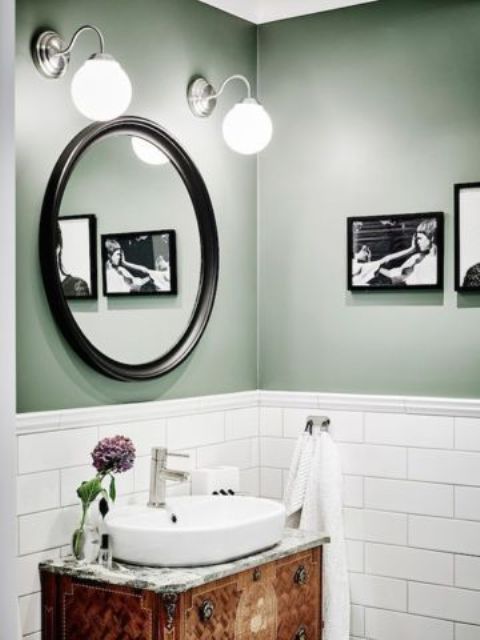 a bathroom with sage green walls, white subway tiles, a stained vanity, an oval sink and a black frame mirror
