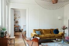 a beautiful Scandinavian living room with a mustard sofa, an amber butterfly chair, a glass coffee table and a bold chandelier