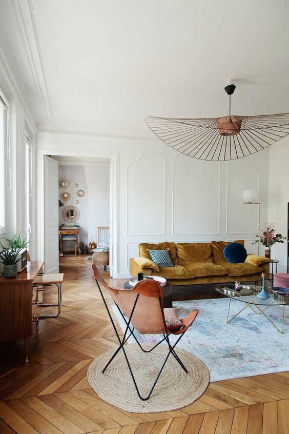 a beautiful Scandinavian living room with a mustard sofa, an amber butterfly chair, a glass coffee table and a bold chandelier