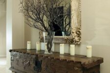 a beautiful and ornated vintage dark-stained trunk on legs, with candles and black branches in a clear vase