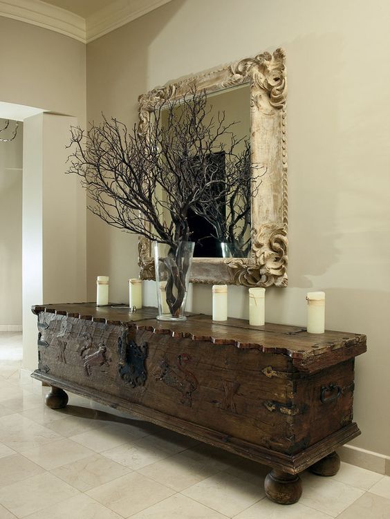 a beautiful and ornated vintage dark-stained trunk on legs, with candles and black branches in a clear vase