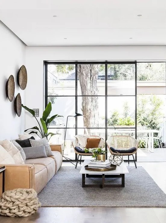 a beautiful living room with a glazed wall, a low tan leather sofa, a low coffee table, rattan chairs and potted plants