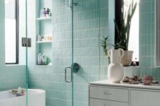 a beautiful mint blue bathroom clad with skinny tiles, with an oval tub, a shower space, a white floating vanity and a large mirror