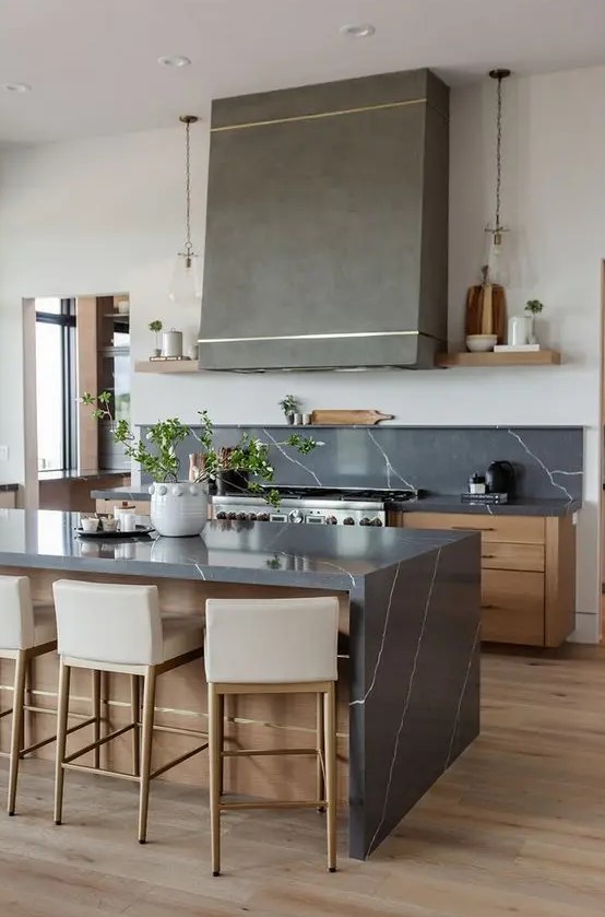 a beautiful stained kitchen with flat panel cabinets, grey soapstone countertops, a grey hood and pendant lamps