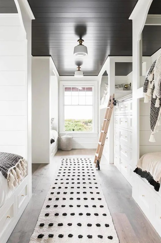 a black and white kids' bedroom with built in usual and bunk beds, with a built in oversized dresser and a ladder
