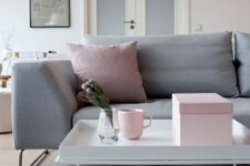 a blush living room with a grey sofa with grey and pink pillows, a coffee table and a grey rug, some pink accessories