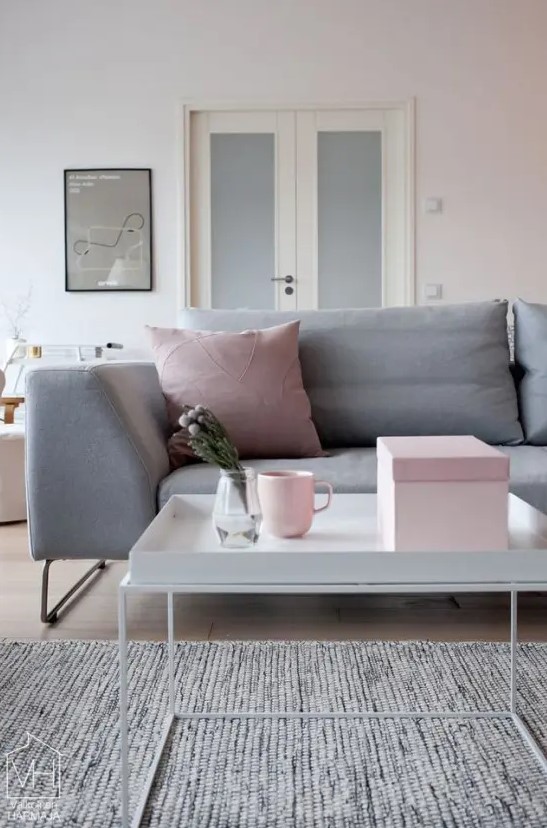 a blush living room with a grey sofa with grey and pink pillows, a coffee table and a grey rug, some pink accessories