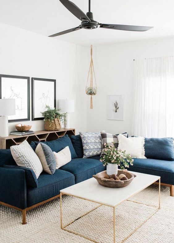 a boho coastal living room with a navy sectional, a coffee table, a console table, potted greenery and artwork