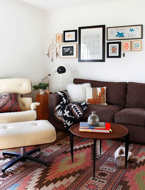 a boho living room with a brown sofa, a creamy Eames chair, a coffee table, bold printed pillows and a rug plus a colorful gallery wall