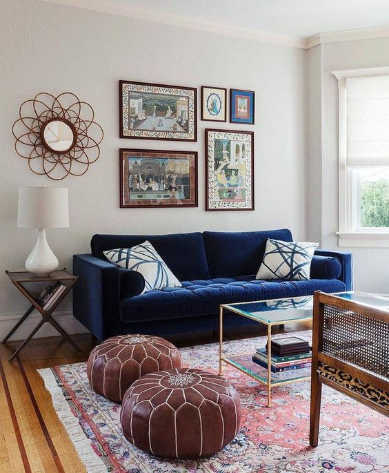 a boho living room with a navy sofa, brown leather poufs, a tiered glass coffee table and a bold gallery wall