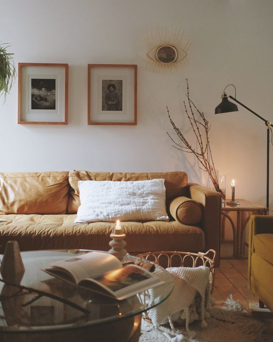 a boho living room with a tan leather sofa, a glass coffee table, a basket with blankets, a black lamp and a mini gallery wall