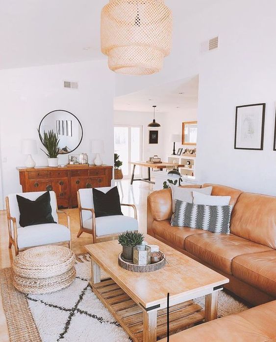 a boho living room with a tan sectional, a coffee table, neutral chairs, a printed rug, jute poufs and a stained credenza
