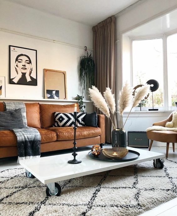 a boho meets Scandinavian living room with a tan leather sofa and a matching chair, a low coffee table on casters, artwork and some decor