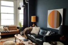 a bold and catchy living room with a black accent wall, a black leather sofa, an amber one, a living edge table, a bulb chandelier