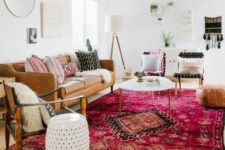 a bold boho living room with a tan leather couch, a bright pink printed rug, some chairs, a coffee table and a leather pouf