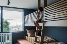 a bold kids’ room with navy walls, multiple bunk beds and a crib, colorful textiles and a bold printed rug
