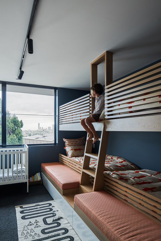 a bold kids' room with navy walls, multiple bunk beds and a crib, colorful textiles and a bold printed rug