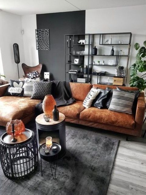 a bold living room with a black accent wlal, a tan leather sectional, black and white pillows, a rug, a storage unit and nightstands