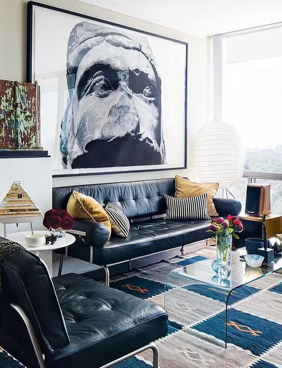 a bold living room with a black leather sofa and a chair, a side table and an acrylic coffee one, a bold print on the wall