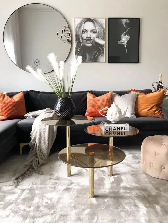 a bold living room with a black sectional, orange pillows, a three tier coffee table, a mirror and some black and white prints on the wall
