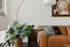 a bright boho living room with a low tan leather sofa, a colorful printed rug, a side table, a bold artwork and greenery