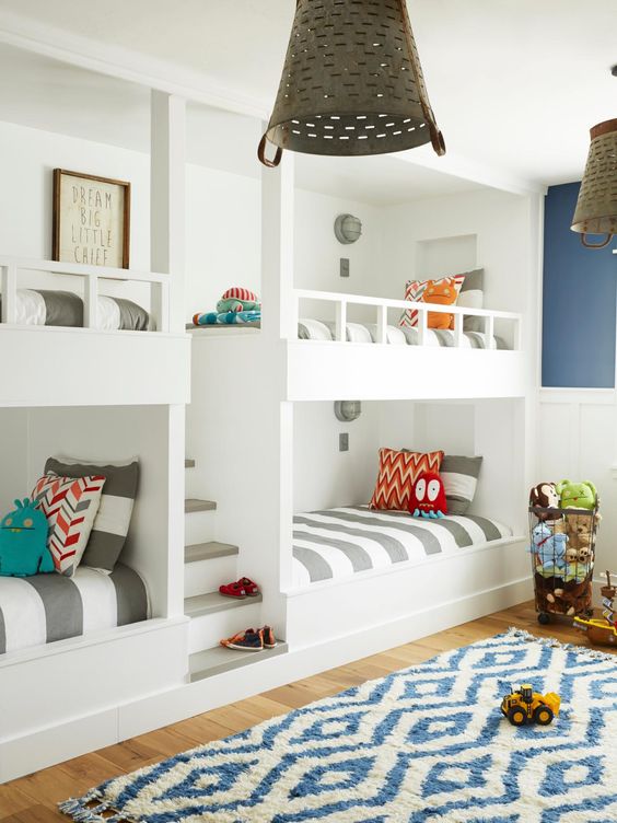a bright kids' bedroom with multiple built-in bunk beds and printed bedding, a printed rug, metal lamps and colorful toys
