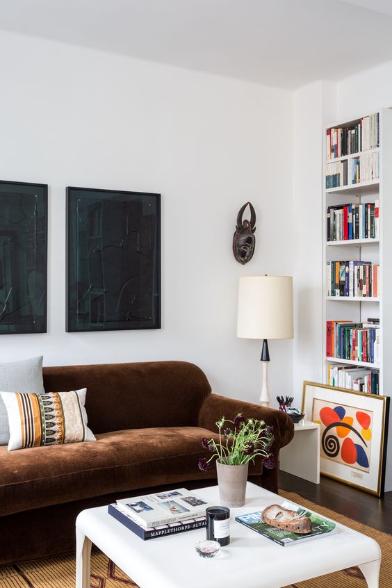 a bright living room with a brown sofa, a white coffee table, a mustard rug, built-in bookshelves and a dark gallery wall