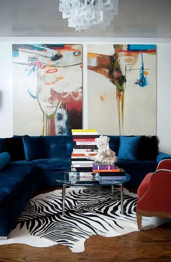 a bright living room with a navy sectional, a red chair, a clear glass coffee table, bold artwork and a zebra print rug is amazing
