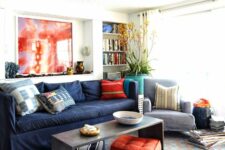 a bright living room with a navy sofa, a coffee table, bold red and orange pillows, a statement plant and a bold rug