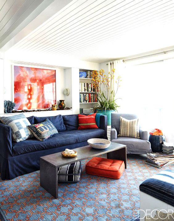 a bright living room with a navy sofa, a coffee table, bold red and orange pillows, a statement plant and a bold rug