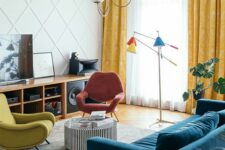 a bright mid-century modern living room with a stained storage unit, a coral and mustard chair, a navy sofa, a side table and colorful lamps