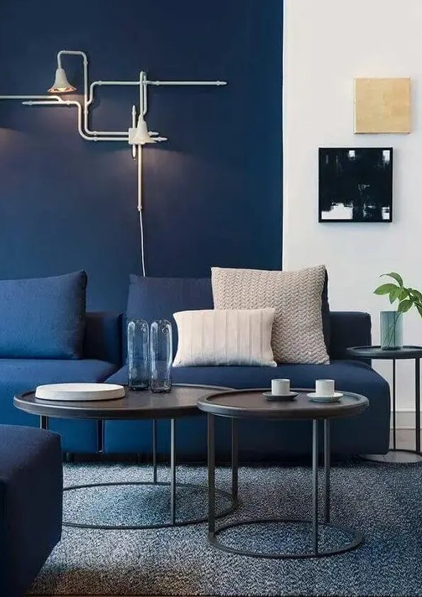 a bright modern living room with navy walls, navy sofas, black side tables and cool art, unique industrial inspired sconces