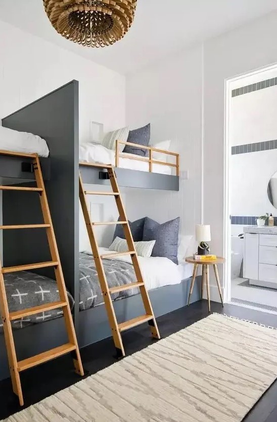 a catchy and contrasting graphite grey and white kids' room with four built in bunk beds, wooden ladders and a side table, a wooden pendant lamp