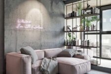 a catchy living room with a low pink sofa and grey pillows, a grey concrete wall with a pink neon sign, a shelving unit